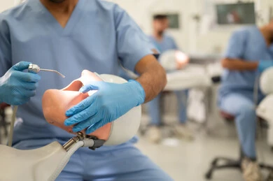 تنظيف وتجديد الأسنان المصابة بالتسوس، صورة مقربة  لطالب جامعي بكلية الأسنان يرتدي القفازات يقوم بفحص مجسم به طاقم أسنان، مفهوم التدريب العملي، المعدات والادوات اللازمة لإجراء الفحوصات, الأساليب العلاجية المتبعة للعناية بالفم