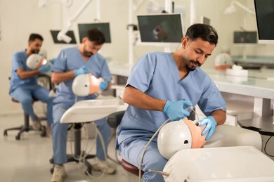 الاستعانة بالأدوات والمعدات السنية أثناء العمل، طرق علاجية للعناية بالأسنان، معالجة التسوس وتركيب الحشوات، مجموعة من الطلاب الجامعيين بكلية الأسنان يرتدون القفازات يقومون بفحص الأسنان على مجسم