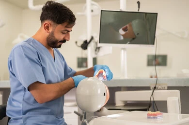 معالجة العيوب الناتجة عن التسوس، طالب جامعي بكلية الأسنان يرتدي القفازات يقوم بفحص مجسم به طاقم أسنان، مفهوم التدريب العملي، المعدات والادوات اللازمة لإجراء الفحوصات, الأساليب العلاجية المتبعة للعناية بالفم