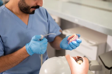 تنظيف تجاويف التسوس، صورة مقربة لطالب جامعي بكلية الأسنان يرتدي القفازات يقوم بفحص مجسم به طاقم أسنان، مفهوم التدريب العملي، المعدات والادوات اللازمة لإجراء الفحوصات, الأساليب العلاجية المتبعة للعناية بالفم
