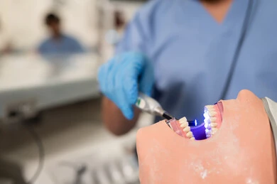 معالجة التسوس وتركيب الحشوات، تصوير مقرب لطالب جامعي عربي خليجي سعودي بكلية الأسنان يرتدي القفازات يقوم بفحص مجسم طاقم أسنان، مفهوم التدريب العملي، استخدام معدات وأدوات طب الأسنان، الأساليب العلاجية المتبعة للعناية بالفم