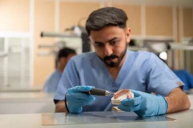 Treatment of dental cavities and placement of restorative fillings, a group of university students in the Faculty of Dentistry wearing gloves examining a dental prosthesis model, use of dental equipment and tools, therapeutic methods used for oral care.