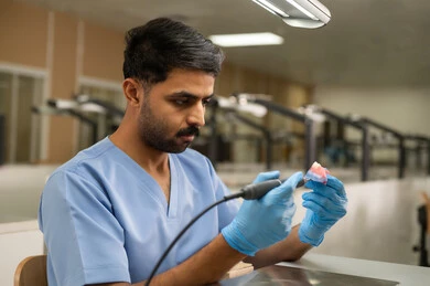 تجهيز حشوات لعلاج الأسنان المتضررة، معالجة الأسنان من التسوس، الأساليب العلاجية المتبعة للعناية بالفم، التعليم الجامعي فى المملكه العربيه السعوديه ، المعدات والادوات اللازمة لإجراء الفحوصات، طالب عربي جامعي سعودي بكلية الأسنان يرتدي القفازات يقوم بنحت طاقم أسنان