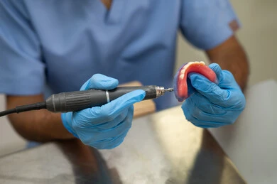 تحضير مواد الحشو للأسنان، الأساليب العلاجية المتبعة للعناية بالفم، التعليم الجامعي فى المملكه العربيه السعوديه ، المعدات والادوات اللازمة لإجراء الفحوصات، صورة مقربة لطالب عربي جامعي سعودي بكلية الأسنان يرتدي القفازات يقوم بنحت طاقم أسنان