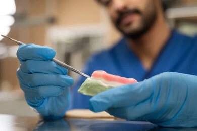 Preparation of fillings for cavity treatment, therapeutic methods used for oral care, higher education in the Kingdom of Saudi Arabia, equipment and tools necessary for conducting examinations, a close-up image of a Saudi Arab university student in the College of Dentistry wearing gloves and sculpting a set of dentures.