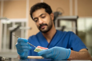 تجهيز الحشوات السنية، معالجة الأسنان من التسوس، الأساليب العلاجية المتبعة للعناية بالفم، التعليم الجامعي فى المملكه العربيه السعوديه ، المعدات والادوات اللازمة لإجراء الفحوصات، صورة مقربة لطالب عربي جامعي سعودي بكلية الأسنان يرتدي القفازات يقوم بنحت طاقم أسنان