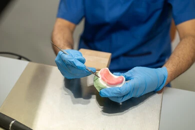 Preparation of dental fillings, treatment of teeth from decay, therapeutic methods used for oral care, higher education in the Kingdom of Saudi Arabia, equipment and tools necessary for conducting examinations, a close-up image of the hand of a Saudi Arabian university student in the dental college wearing gloves and sculpting a dental prosthesis.