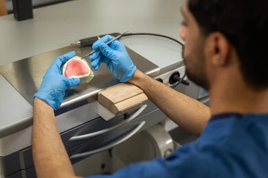 معالجة تسوس الأسنان بشكل عملي، مفهوم التدريب العملي، المعدات والادوات اللازمة لإجراء الفحوصات، صورة مقربة لطالب عربي خليجي سعودي بكلية الأسنان يرتديان القفازات يقوم بفحص طاقم أسنان، الأساليب العلاجية المتبعة للعناية بالفم