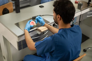 Treatment of dental damage caused by decay, the concept of practical training, the equipment and tools necessary for conducting examinations, a close-up image of a Saudi Gulf Arab dental student wearing gloves examining a set of teeth, the therapeutic methods used for oral care.