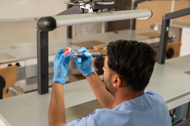 إزالة النخر وعلاج الأسنان المتسوسة، مفهوم التدريب العملي، المعدات والادوات اللازمة لإجراء الفحوصات، صورة مقربة لطالب عربي خليجي سعودي بكلية الأسنان يرتديان القفازات يقوم بفحص طاقم أسنان، الأساليب العلاجية المتبعة للعناية بالفم