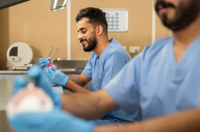 المعدات والادوات اللازمة لإجراء الفحوصات، معالجة النخر والتسوس، صورة مقربة من الجانب لطالبان عربيان خليجيان سعوديان بكلية الأسنان يرتديان القفازات يقومان بفحص طاقم أسنان، مفهوم التدريب العملي، الأساليب العلاجية المتبعة للعناية بالفم