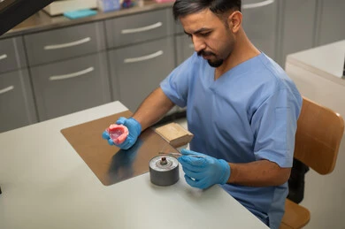 Preparation of dental fillings, treatment of teeth from decay, therapeutic methods used for oral care, higher education in the Kingdom of Saudi Arabia, equipment and tools necessary for conducting examinations, a Saudi Arab university student in the College of Dentistry wearing gloves is sculpting a set of dentures.