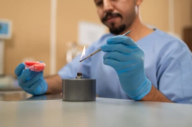 معالجة الأسنان من التسوس، الأساليب العلاجية المتبعة للعناية بالفم، التعليم الجامعي فى المملكه العربيه السعوديه ، المعدات والادوات اللازمة لإجراء الفحوصات، صورة مقربة لطالب عربي جامعي سعودي  بكلية الأسنان يرتدي القفازات يقوم بنحت طاقم أسنان