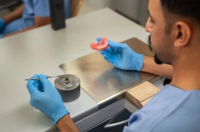 معالجة التسوس وتركيب الحشوات، التعليم الجامعي فى المملكه العربيه السعوديه ، المعدات والادوات اللازمة لإجراء الفحوصات، الأساليب العلاجية المتبعة للعناية بالفم، صورة مقربة  من الجانب طالب عربي جامعي سعودي  بكلية الأسنان يرتدي القفازات يقوم بنحت طاقم أسنان