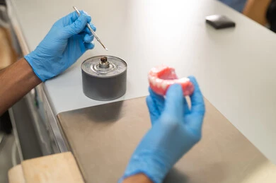 التعليم الجامعي فى المملكه العربيه السعوديه ، المعدات والادوات اللازمة لإجراء الفحوصات، معالجة التسوس وتركيب الحشوات، الأساليب العلاجية المتبعة للعناية بالفم، صورة مقربة  ليد طالب عربي جامعي سعودي  بكلية الأسنان يرتدي القفازات يقوم بنحت طاقم أسنان