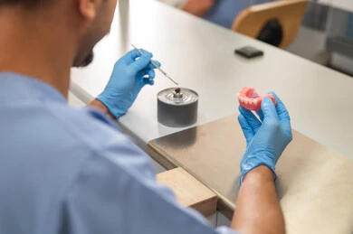 المعدات والادوات اللازمة لإجراء الفحوصات، التعليم الجامعي فى المملكه العربيه السعوديه ، معالجة التسوس وتركيب الحشوات، الأساليب العلاجية المتبعة للعناية بالفم، صورة مقربة من الخلف لطالب عربي جامعي سعودي  بكلية الأسنان يرتدي القفازات يقوم بنحت طاقم أسنان