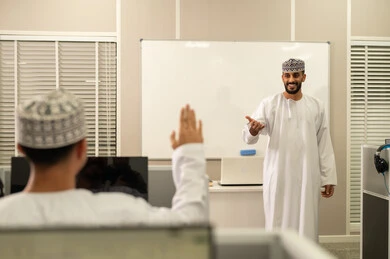 رفع اليدين للمشاركة و التفاعل، الإستماع الى المحاضره، أستاذ جامعي عربي خليجي عماني يرتدي الدشداشة و الكمة يشرح لطلابه في المحاضره, جامعات أكاديميه في سلطنه عمان , كليات وجامعات متطوره