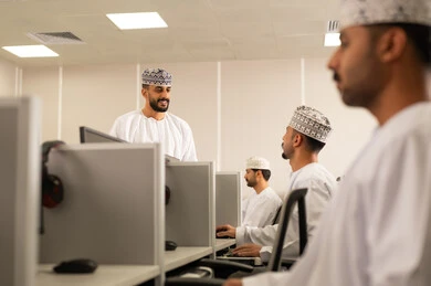 تدريب وورش تعليمية، التعليم الجامعي العماني، تطوير أساليب التعليم الجامعي في سلطنه عمان، طالب عربي خليجي عماني يرتدي الدشداشة و الكمة يجلس امام الحاسوب يقوم بالمناقشة مع المعلم