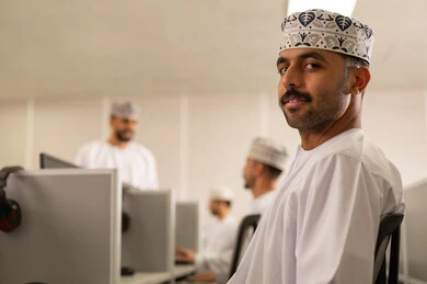 Omani higher education, workshops and training courses, developing university teaching methods in the Sultanate of Oman, an Arab Gulf Omani student wearing a dishdasha and kumma sitting in front of the computer discussing with the teacher.