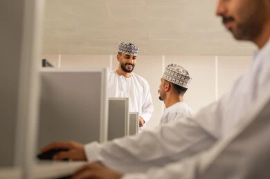 تطوير أساليب التعليم الجامعي في سلطنه عمان، طالب عربي خليجي عماني يرتدي الدشداشة و الكمة يجلس امام الحاسوب يقوم بالمناقشة مع المعلم، ورش عمل ودورات تدريبية، التعليم الجامعي العماني