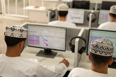 University learning using technology, achievement and excellence in the university stage, a picture from behind of a group of Arab Gulf Omani students wearing the dishdasha and kumma sitting in front of a computer, academic universities in the Sultanate of Oman.