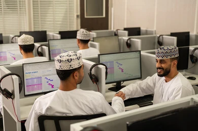 Hand gestures indicating a handshake, discussing study materials, pointing to something, teamwork and collaboration among colleagues, online study at the university, achievement and excellence in the university stage, a group of Arab Gulf Omani students wearing the dishdasha and kumma sitting in front of the computer.