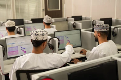 مناقشة المواد الدراسيه، الاشارة الى شاشة الكمبيوتر، العمل الجماعي والتعاون بين الزملاء، الدراسة الالكترونية في الجامعة، الانجاز و التفوق في المرحلة الجامعية، مجموعه من الطلاب العربيون الخليجيون العمانيون يرتدون الدشداشة و الكمة يجلسون امام الحاسوب