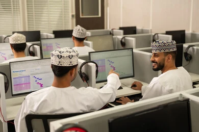 Referring to the computer screen, discussing study materials, teamwork and collaboration among colleagues, electronic study at the university, achievement and excellence in the university stage, a group of Arab Gulf students from Oman wearing the dishdasha and kumma sitting in front of the computer.