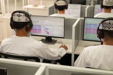 التعليم عبر الكمبيوتر الجامعي، الانجاز و التفوق في المرحلة الجامعية، صورة من الخلف لمجموعه من الطلاب العربيون الخليجيون العمانيون يرتدون الدشداشة و الكمة يقومون بالنظر الى الحاسوب بايماءات الاندماج و التركيز، استخدام تقنية الهيدفون فى التعليم