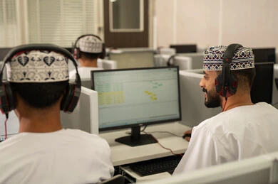 الحصص الدراسية عبر الكمبيوتر، الانجاز و التفوق في المرحلة الجامعية، صورة من الخلف لمجموعه من الطلاب العربيون الخليجيون العمانيون يرتدون الدشداشة و الكمة يقومون بالنظر الى الحاسوب بايماءات الاندماج و التركيز، استخدام تقنية الهيدفون فى التعليم