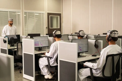 Using headphones while studying, academic universities in the Sultanate of Oman, a picture from behind of Omani students sitting in front of the computer listening to the lecture, an Arab Gulf university professor from Oman wearing a dishdasha and kumma explaining to his students in the lecture, advanced colleges and universities.