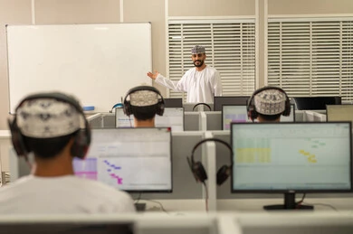 الاستماع عبر سماعات هيدفون، صورة من الخلف لطلاب عمانوين يجلسون امام الحاسوب يقومون بالإستماع الى المحاضره، أستاذ جامعي عربي خليجي عماني يرتدي الدشداشة و الكمة يشرح لطلابه في المحاضره, جامعات أكاديميه في سلطنه عمان , كليات وجامعات متطوره الاستماع عبر سماعات هيدفون، صورة من الخلف لطلاب عمانوين يجلسون امام الحاسوب يقومون بالإستماع الى المحاضره، أستاذ جامعي عربي خليجي عماني يرتدي الدشداشة و الكمة يشرح لطلابه في المحاضره, جامعات أكاديميه في سلطنه عمان , كليات وجامعات متطوره