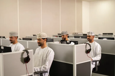 التعلم الإلكتروني بالجامعة ، مجموعة من الطلاب العربيون الخليجيون العمانوين يرتدون الدشداشة والكمه يجلسون أمام أجهزة الكمبيوتر في مختبر حديث، التركيز على الدراسة والتفاعل الأكاديمي