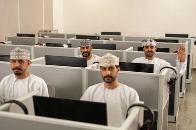 التعليم عبر الحاسوب الجامعي، مجموعة من الطلاب العربيون الخليجيون العمانوين يرتدون الدشداشة والكمه يجلسون أمام أجهزة الكمبيوتر في مختبر حديث، التركيز على الدراسة والتفاعل الأكاديمي