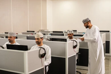 Excellence through diligence and perseverance, an Emirati Gulf Arab teacher wearing a kandura and ghutrah is explaining something, academic universities in the Sultanate of Oman, a group of Omani students sitting in front of the computer listening to the lecture, advanced colleges and universities.