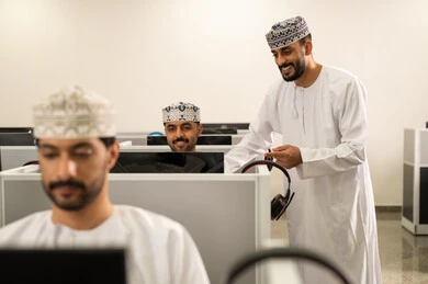 Diligence and the pursuit of excellence, an Emirati Gulf Arab teacher wearing a kandura and ghutrah is explaining something, academic universities in the Sultanate of Oman, a group of Omani students sitting in front of the computer listening to the lecture, advanced colleges and universities.