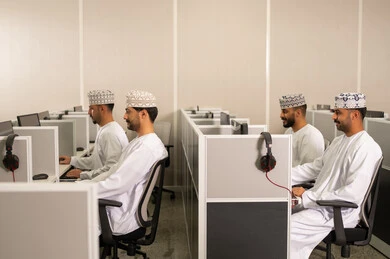 الدراسة الرقمية في الجامعة، مجموعة من الطلاب العربيون الخليجيون العمانوين يرتدون الدشداشة والكمه يجلسون أمام أجهزة الكمبيوتر في مختبر حديث، التركيز على الدراسة والتفاعل الأكاديمي