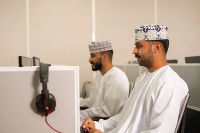 استخدام الحاسوب للتعلم الجامعي، مجموعة من الطلاب العربيون الخليجيون العمانوين يرتدون الدشداشة والكمه يجلسون أمام أجهزة الكمبيوتر في مختبر حديث، التركيز على الدراسة والتفاعل الأكاديمي