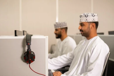 التعليم الإلكتروني في الجامعة، مجموعة من الطلاب العربيون الخليجيون العمانوين يرتدون الدشداشة والكمه يجلسون أمام أجهزة الكمبيوتر في مختبر حديث، التركيز على الدراسة والتفاعل الأكاديمي