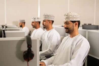 الدراسة عبر الحاسوب الجامعي، مجموعة من الطلاب العربيون الخليجيون العمانوين يرتدون الدشداشة والكمه يجلسون أمام أجهزة الكمبيوتر في مختبر حديث، التركيز على الدراسة والتفاعل الأكاديمي