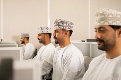 التركيز على الدراسة والتفاعل الأكاديمي، التعلم عبر الحاسوب في الجامعة، مجموعة من الطلاب العربيون  الخليجيون العمانوين يرتدون الدشداشة والكمه يجلسون أمام أجهزة الكمبيوتر في مختبر حديث