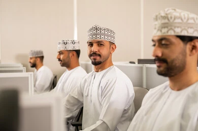 التعلم عبر الحاسوب في الجامعة، مجموعة من الطلاب العربيون الخليجيون العمانوين يرتدون الدشداشة والكمه يجلسون أمام أجهزة الكمبيوتر في مختبر حديث، التركيز على الدراسة والتفاعل الأكاديمي