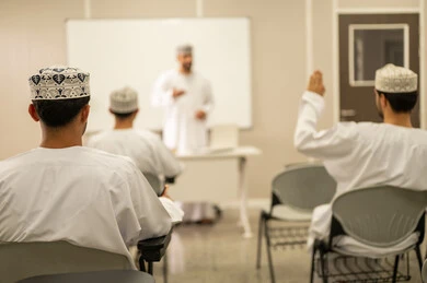 التفاعل مع المعلم و التلاميذ أثناء المحاضرات الدراسية، معلم عربي خليجي عماني يرتدي الدشداشة و الكمة يقوم بشرح الدرس للطلاب، التعليم في سلطنه عمان، مجموعه من الطلاب يستمعون الى الدرس بايماءات الاندماج و التركيز