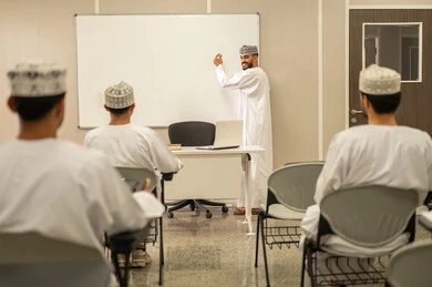 التفاعل والمشاركة داخل الفصل الدراسي، معلم عربي خليجي عماني يرتدي الدشداشة و الكمة يقوم بشرح الدرس للطلاب، التعليم في سلطنه عمان، مجموعه من الطلاب يستمعون الى الدرس بايماءات الاندماج و التركيز