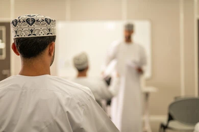 السعي لتحقيق التميز من خلال التعلم, مجموعة من التلاميذ العمانيين يقومون بالاستعداد لحل أسئلة الامتحان, اهداف التربية و التعليم, التعليم في سلطنه عمان , معلم عربي خليجي عماني يرتدي الدشداشة و الكمه يقوم بتوزيع ورق الامتحان على الطلاب