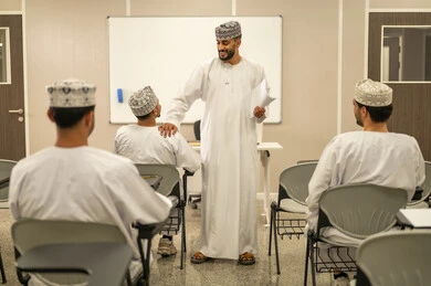 الاجتهاد الأكاديمي لتحقيق التميز, مجموعة من التلاميذ العمانيين يقومون بالاستعداد لحل أسئلة الامتحان, اهداف التربية و التعليم, التعليم في سلطنه عمان ,معلم عربي خليجي عماني يرتدي الدشداشة و الكمه يقوم بتوزيع ورق الامتحان على الطلاب