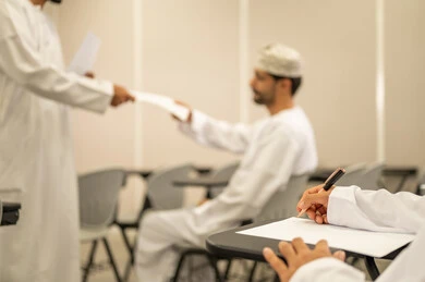 الدراسة و الاجتهاد من اجل التفوق, مجموعة من التلاميذ العمانيين يقومون بالاستعداد لحل أسئلة الامتحان, اهداف التربية و التعليم, التعليم في سلطنه عمان ,معلم عربي خليجي عماني يرتدي الدشداشة و الكمه يقوم بتوزيع ورق الامتحان على الطلاب