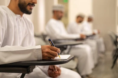 Education in the Sultanate of Oman, striving in studies to achieve success and academic excellence, a close-up image of an Arab Gulf Omani student writing, the goals of education and teaching, a group of students solving exam questions.