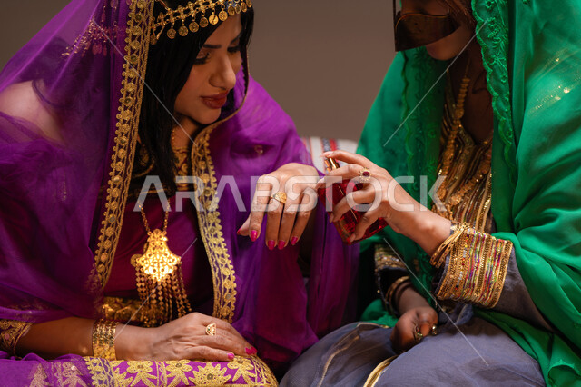 مسح المسك على يد العروس عطور ذات روائح مميزة، احتفالات سعيدة ومناسبات وأفراح، الاهتمام والعناية بالأناقة والجمال، منتجات ومساحيق التجميل، صورة مقربة لسيداتان عربيتان خليجيتان اماراتيتان يقومون بعرض الفساتين والمجوهرات، إيماءات السعادة والفرح ، الاحتفال بليلة العمر