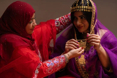 Assistance in wearing the golden attire at weddings, happy celebrations, occasions, and festivities, attention and care for elegance, beauty products and cosmetics, a close-up image of two Emirati Gulf Arab women showcasing the preparations and arrangements for the wedding, gestures of happiness and joy, celebrating the night of a lifetime.
